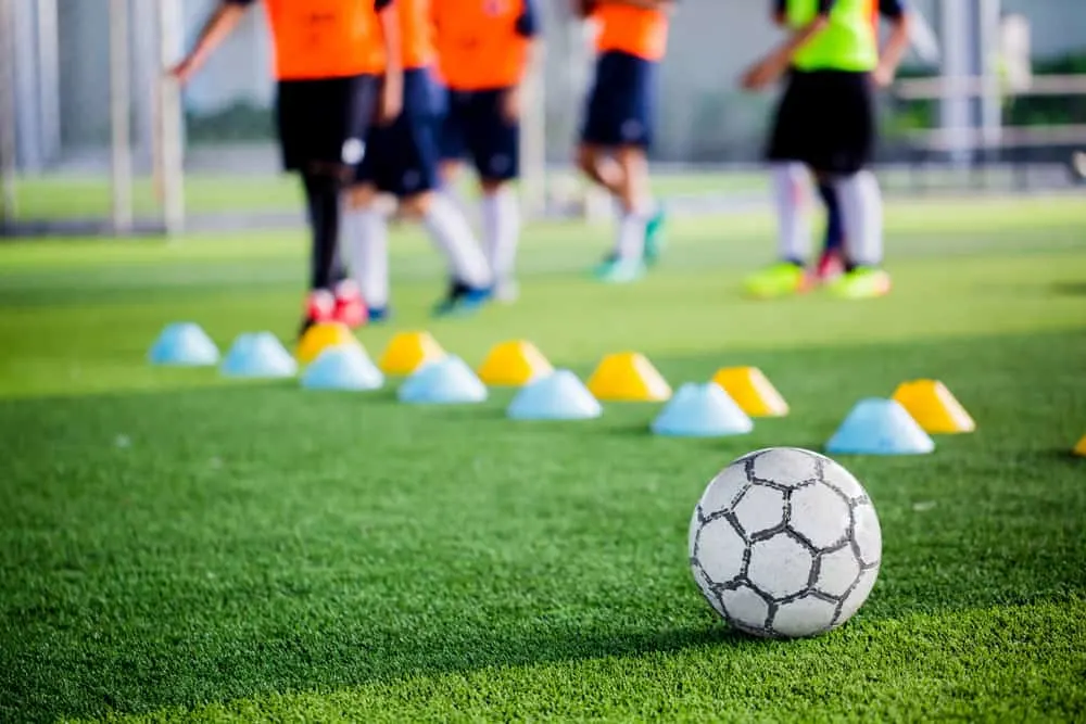 Soccer ball on green artificial turf with blurry of maker cones and players training